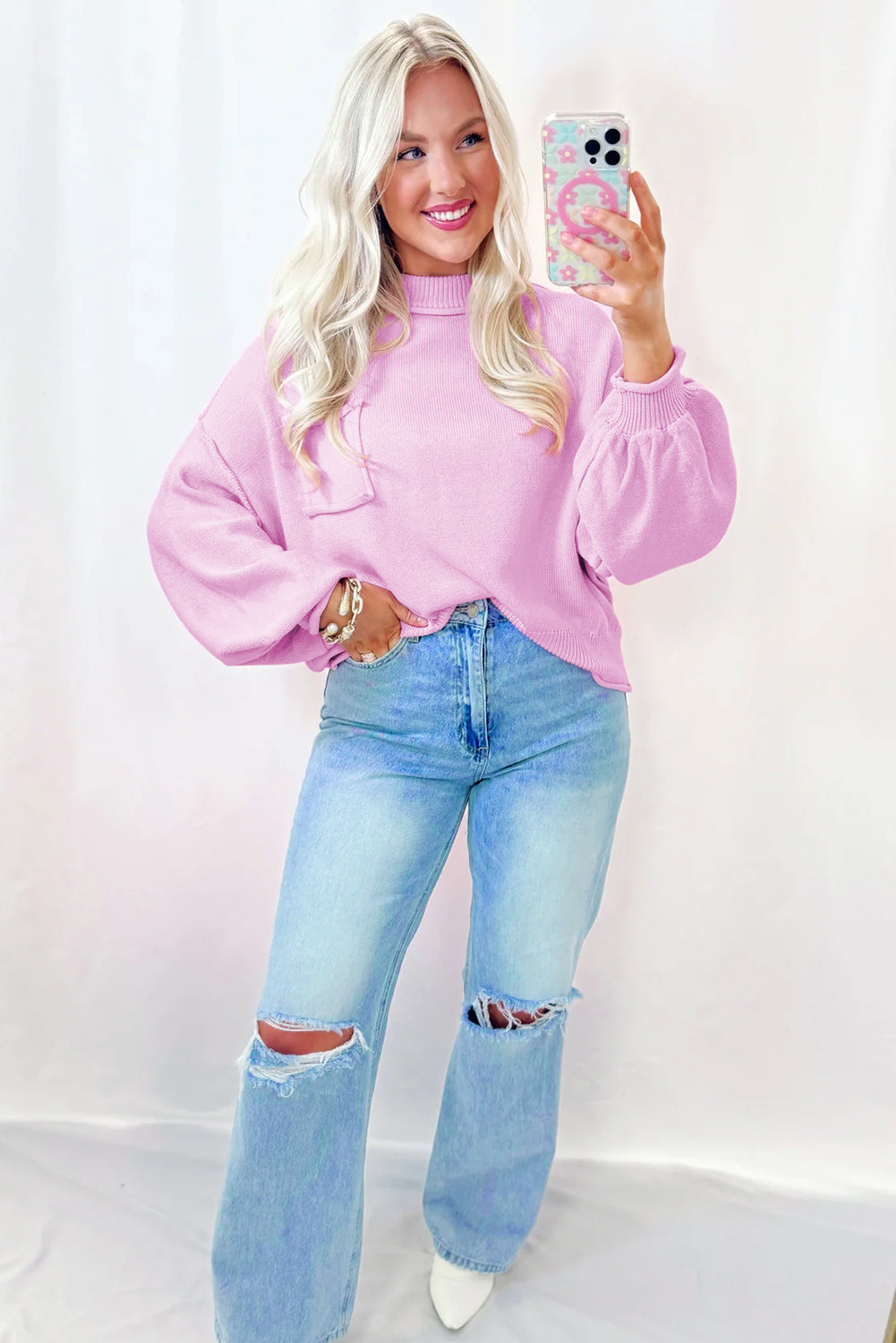 Person wearing a pink sweater and light blue jeans against a white background